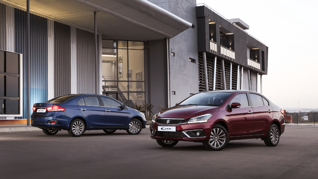 A blue and red Suzuki Ciaz parked next to a commercial building