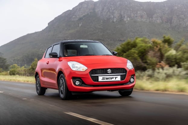 Red Suzuki Swift driving on the road near the mountains