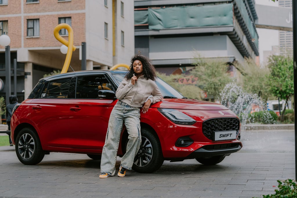 red suzuki swift with woman standing in front of it