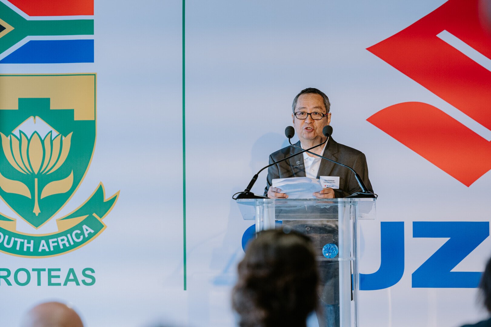 Man speaking at a podium in front of Suzuki logo