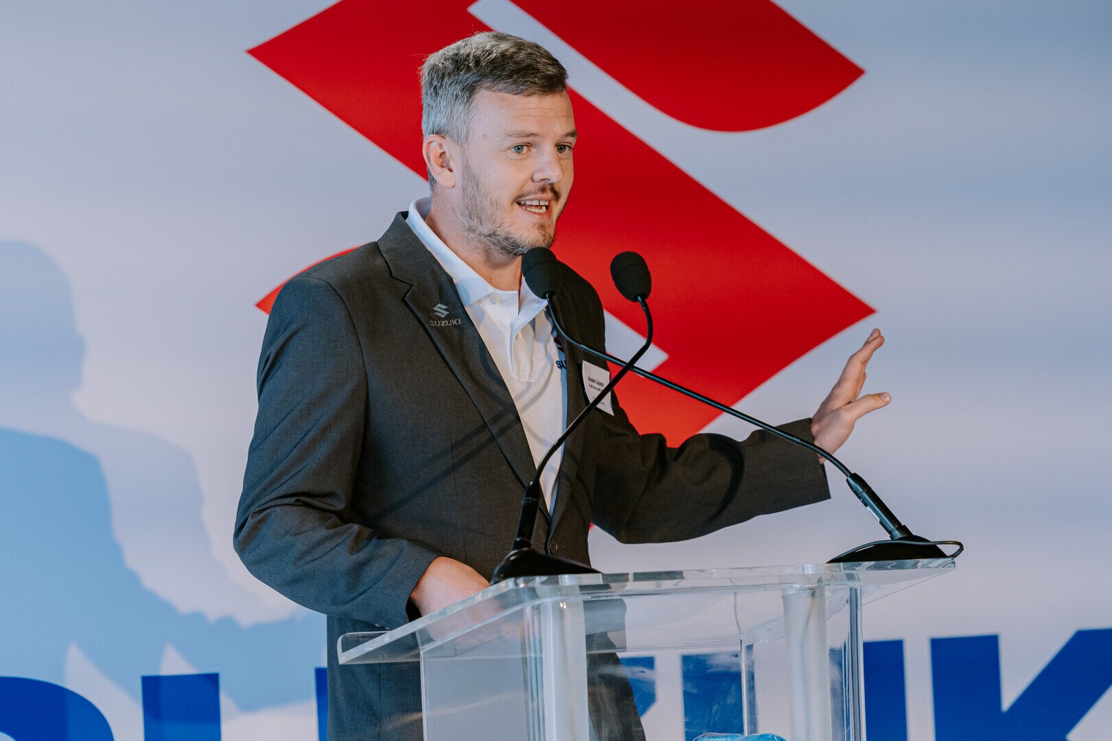 Man speaking at a podium in front of Suzuki logo