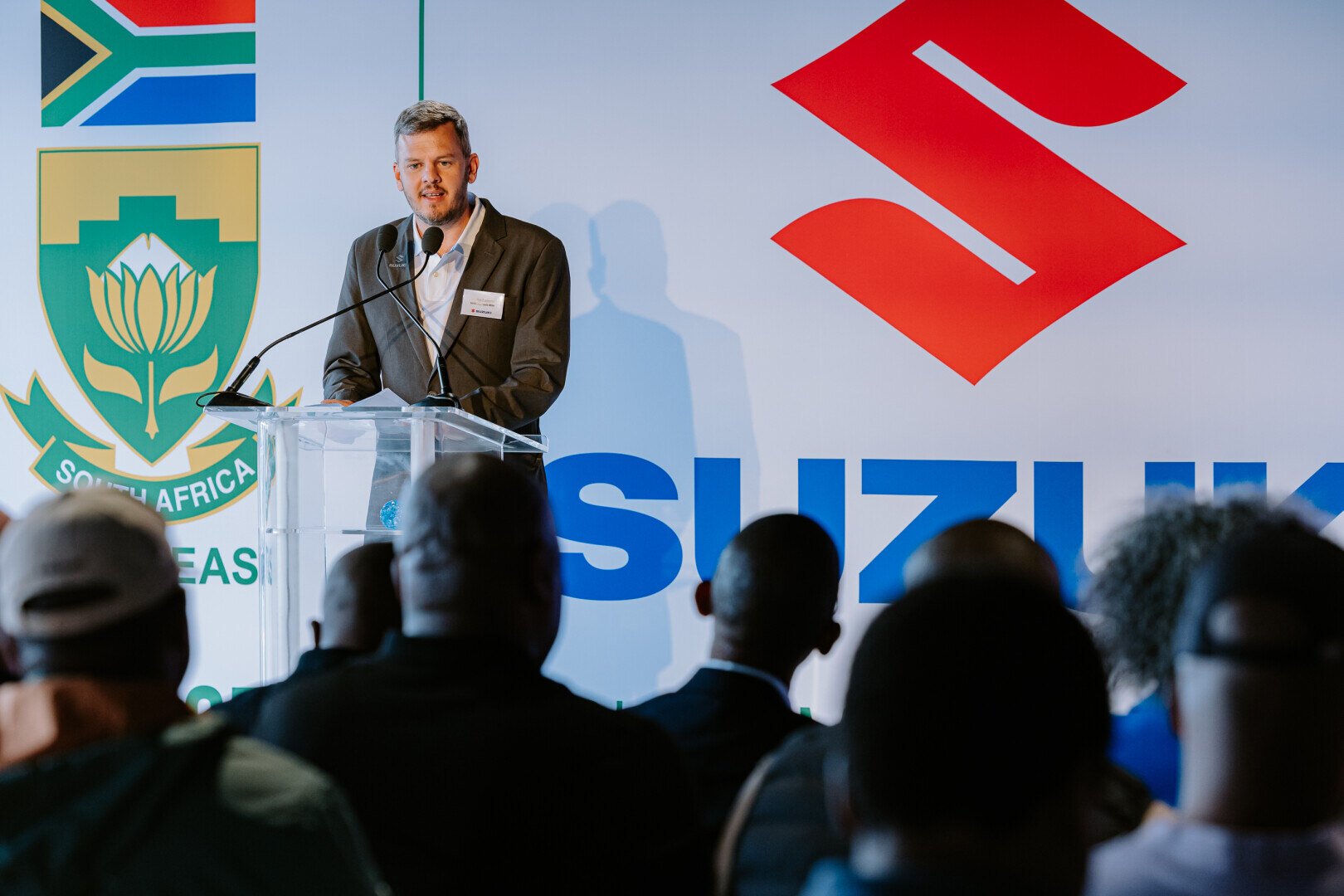 Man speaking at a podium in front of Suzuki logo