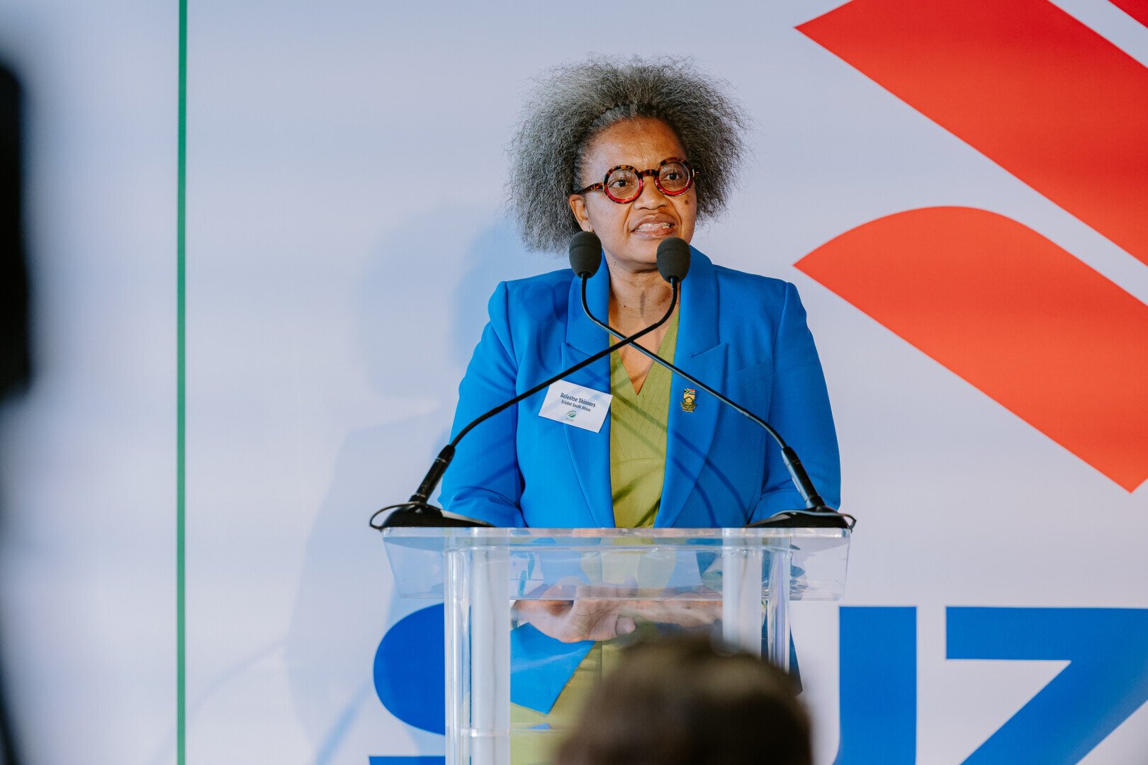 Woman speaking at a podium in front of Suzuki logo