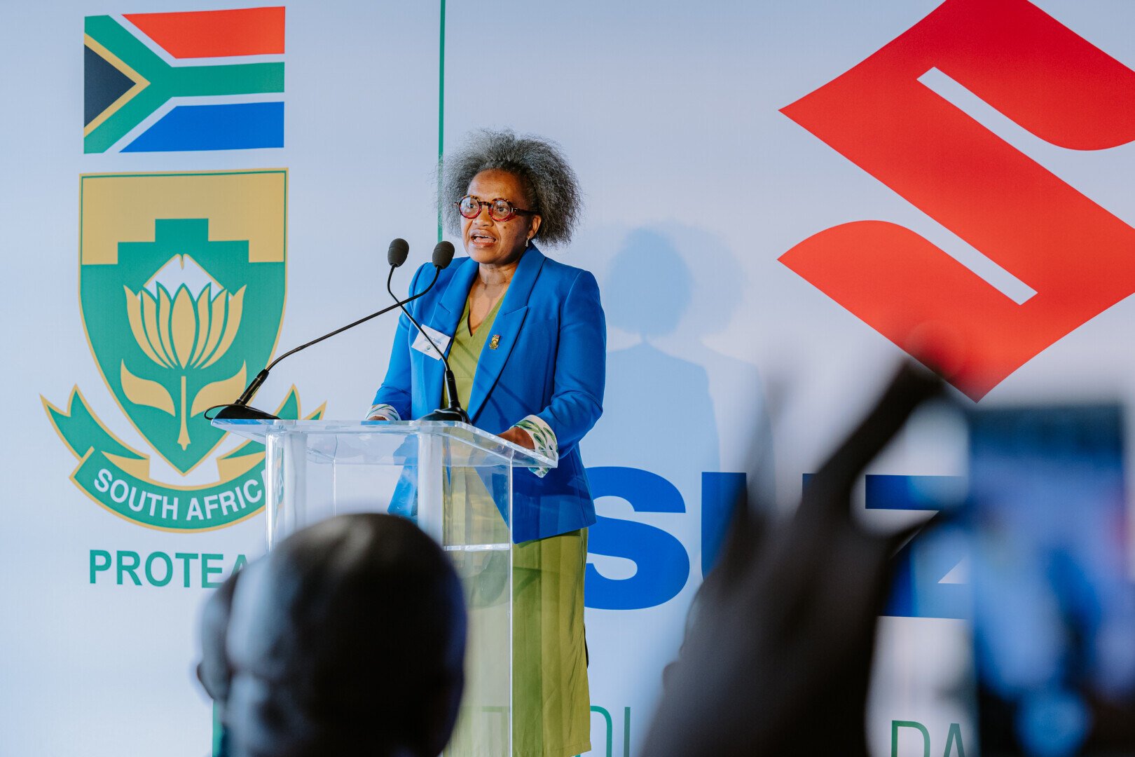 Woman speaking at a podium in front of Suzuki logo