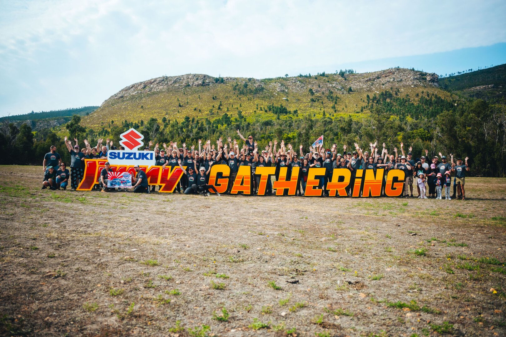 A group of people standing behing a Jimny Gathering sign